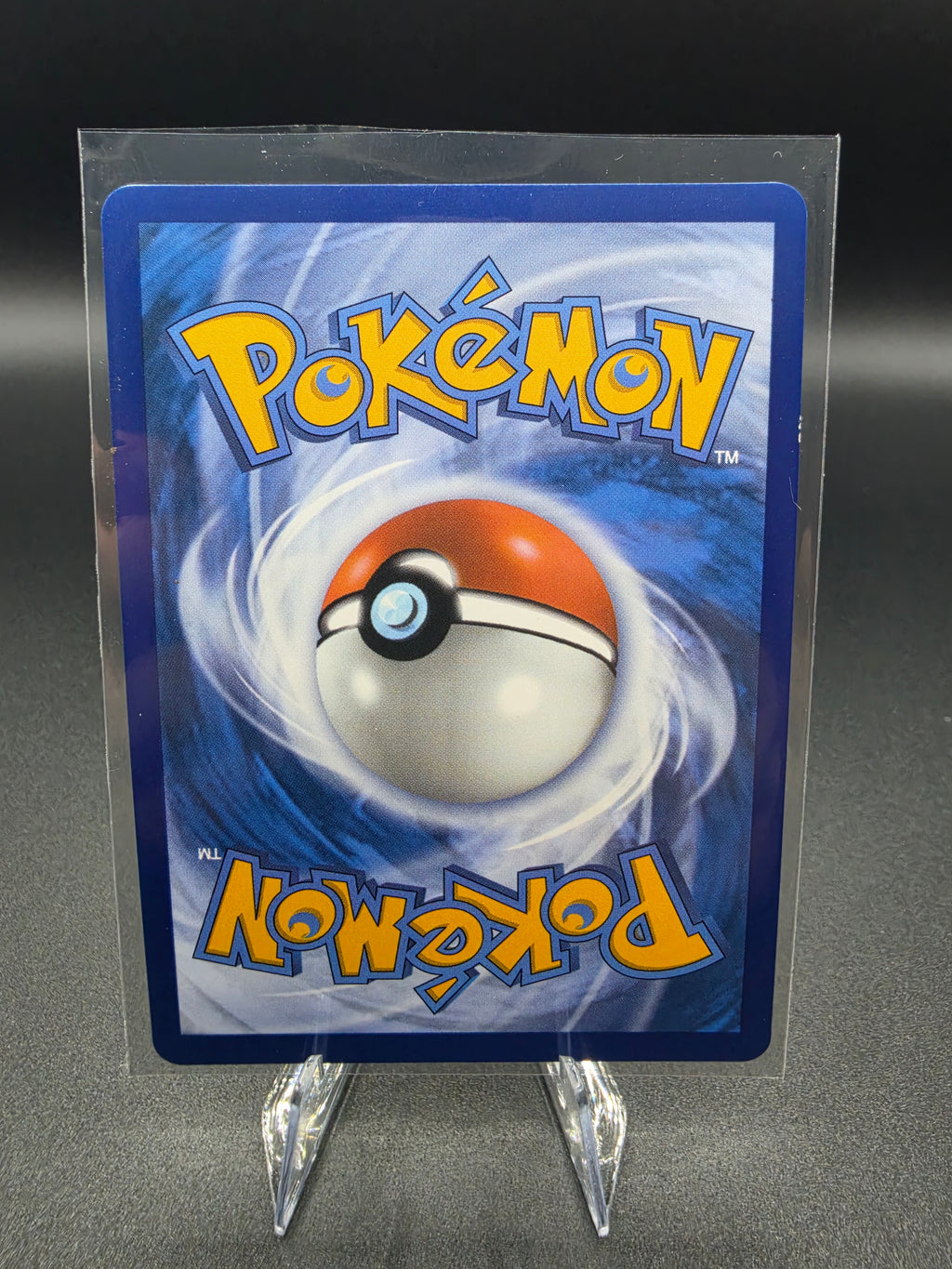 A Pokémon trading card featuring the blue and orange Pokémon logo and a Pokémon Ball graphic, displayed upright in a clear protective sleeve on a small clear stand against a dark gray background.