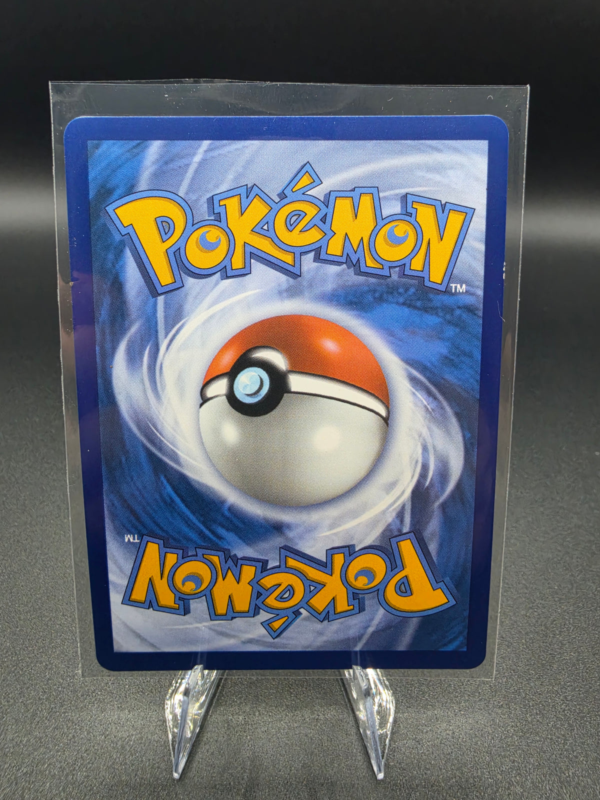 A Pokémon trading card featuring the blue and orange Pokémon logo and a Pokémon Ball graphic, displayed upright in a clear protective sleeve on a small clear stand against a dark gray background.